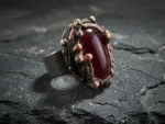 Крупное авторское кольцо с бордовым корундом из текстурированной меди на фоне черного сланца.
